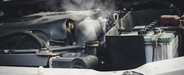 An image of a vehicle engine compartment. There is white steam coming out of the cooling system.