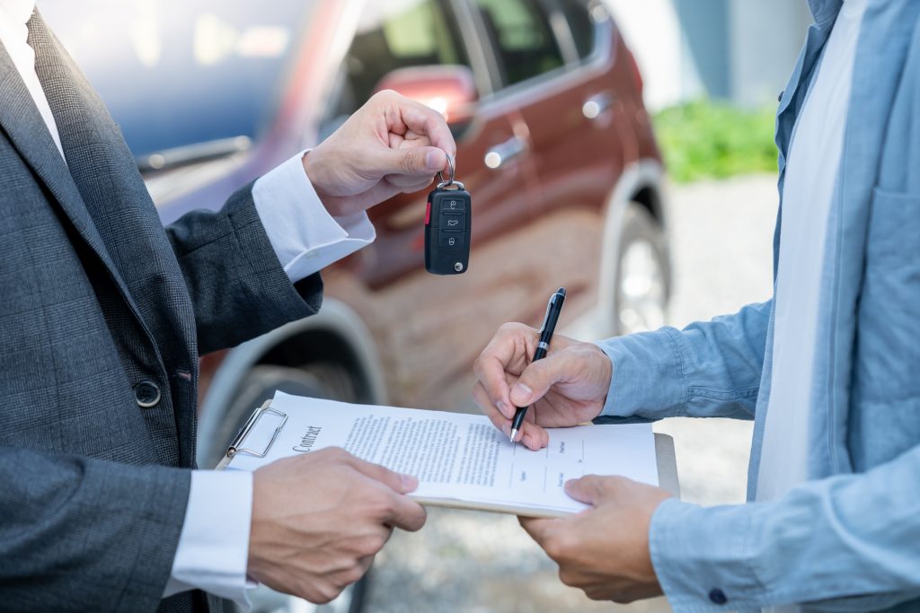 A person signing a car contract and receiving the car keys after purchase.