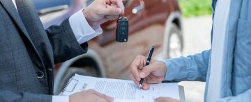 A person signing a car contract and receiving the car keys after purchase.