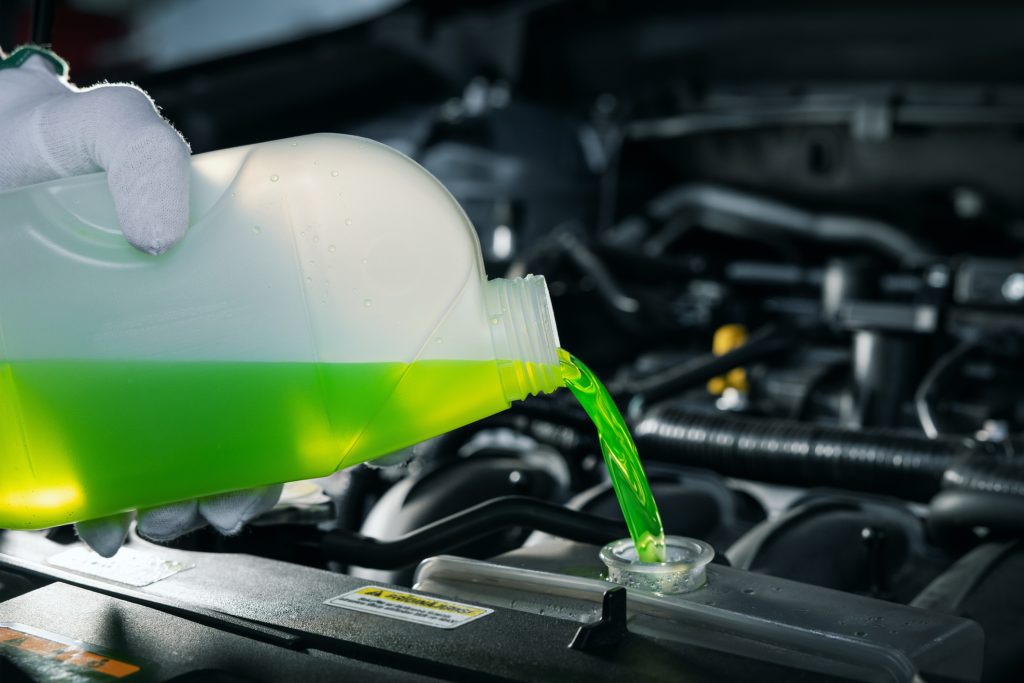 Pouring fresh green engine coolant into a car radiator after flushing the cooling system