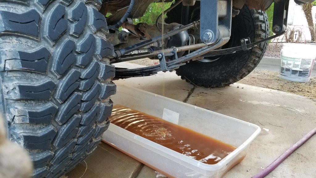 Draining old antifreeze from a vehicle radiator into a plastic drain pan during a cooling system flush